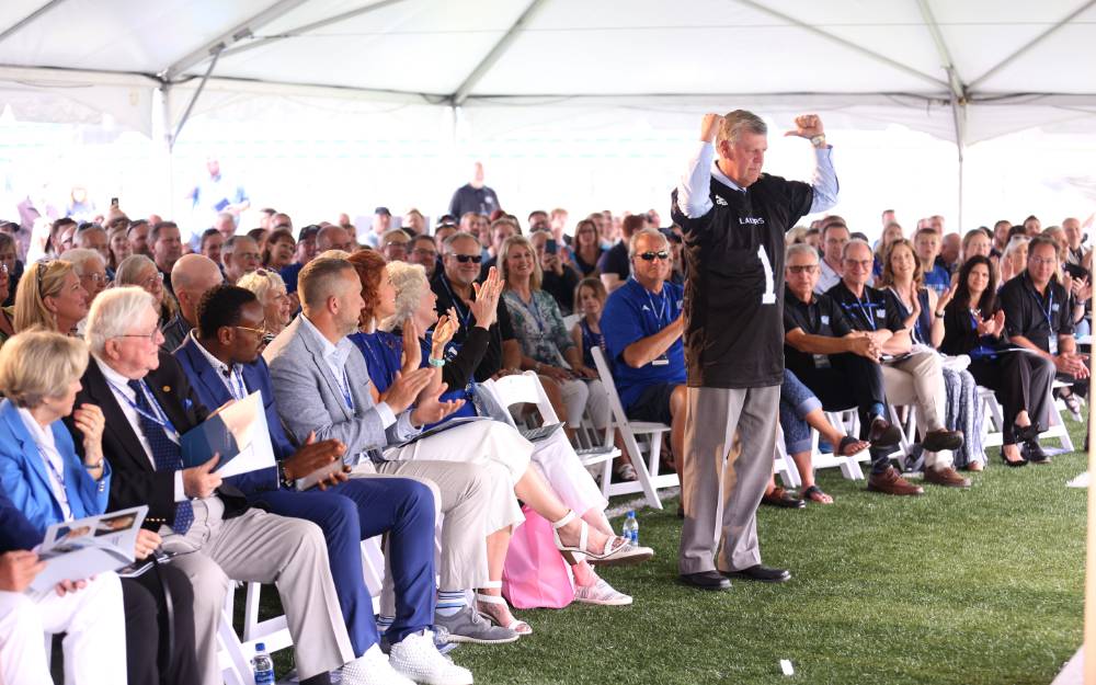 President Tom Haas in front of the crowd at the Jamie Hosford Football Center dedication, pointing to the back of the jersey with his thumbs.